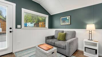 A room with a grey sofa, a wooden tray, a wicker basket, a lamp, and a window with blinds.
