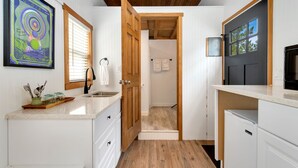 A compact kitchen with white cabinetry, a wooden ceiling, and a door leading to a shower area. - Riverside Colorado (Bellvue)