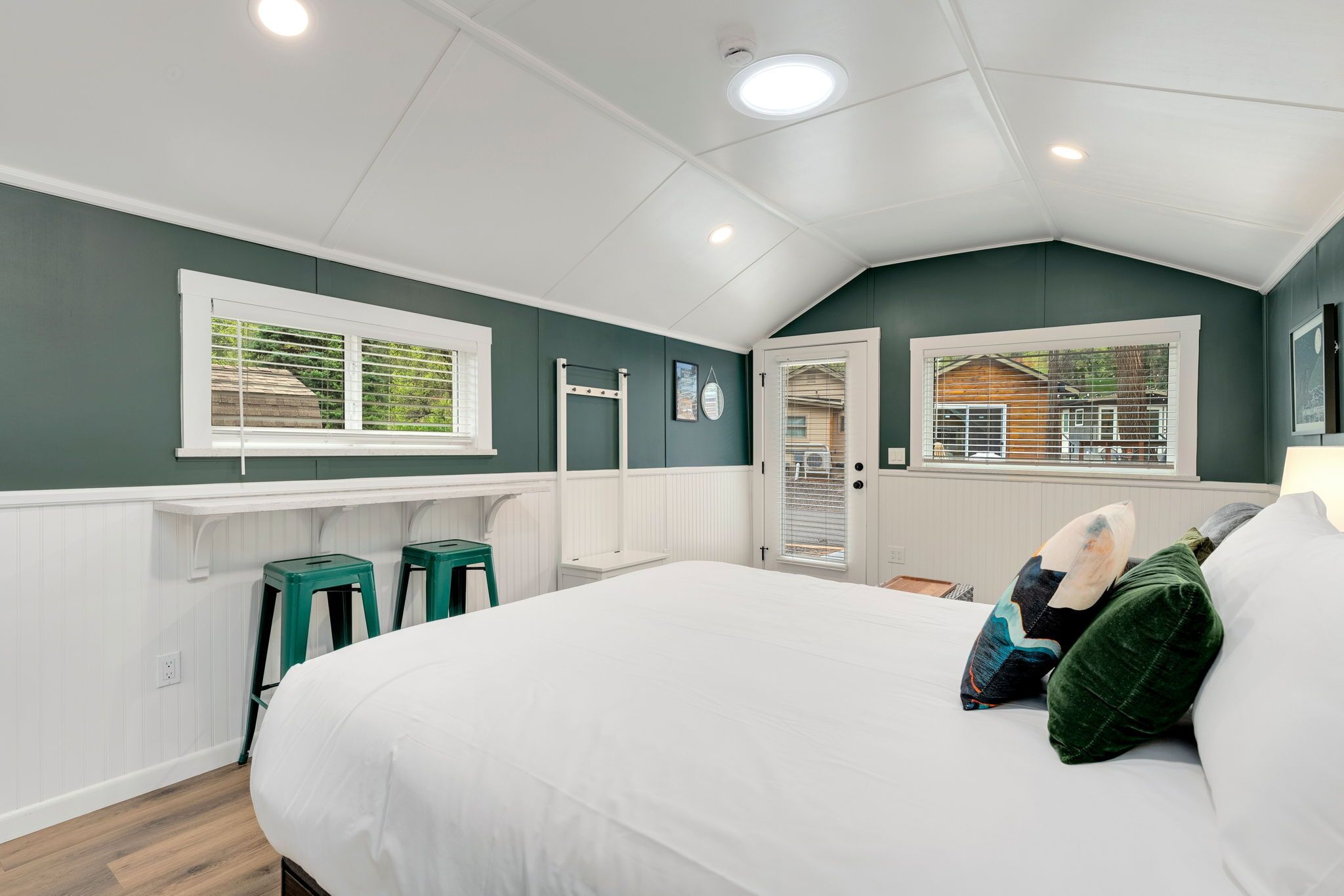 Una camera da letto con un letto, due sgabelli verdi, una finestra e una porta che dà su un balcone.