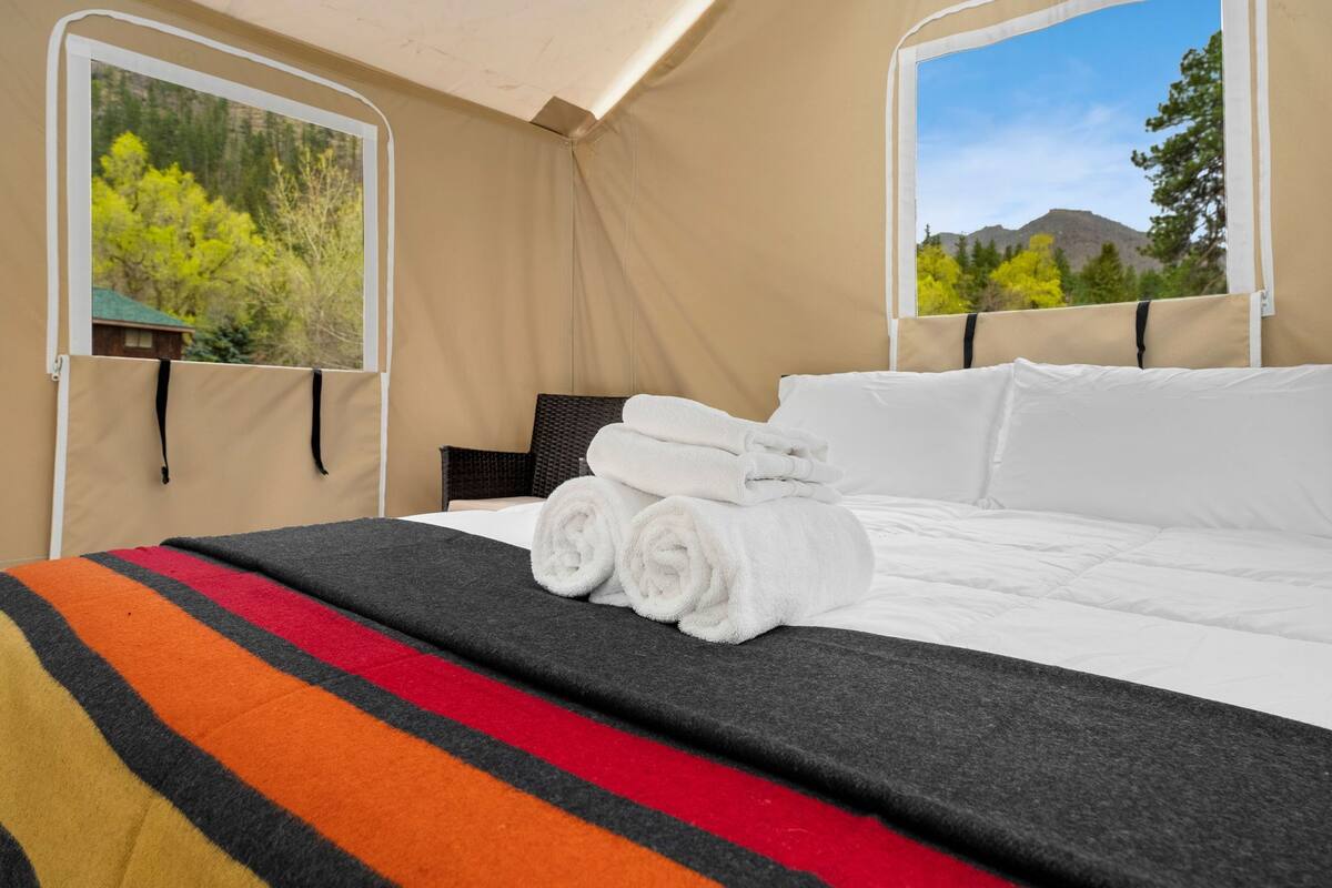 A bed with rolled white towels, a striped blanket, and a view of trees and mountains through a window.