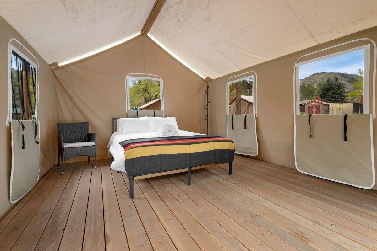 A tented room with a bed, a chair, and two windows.