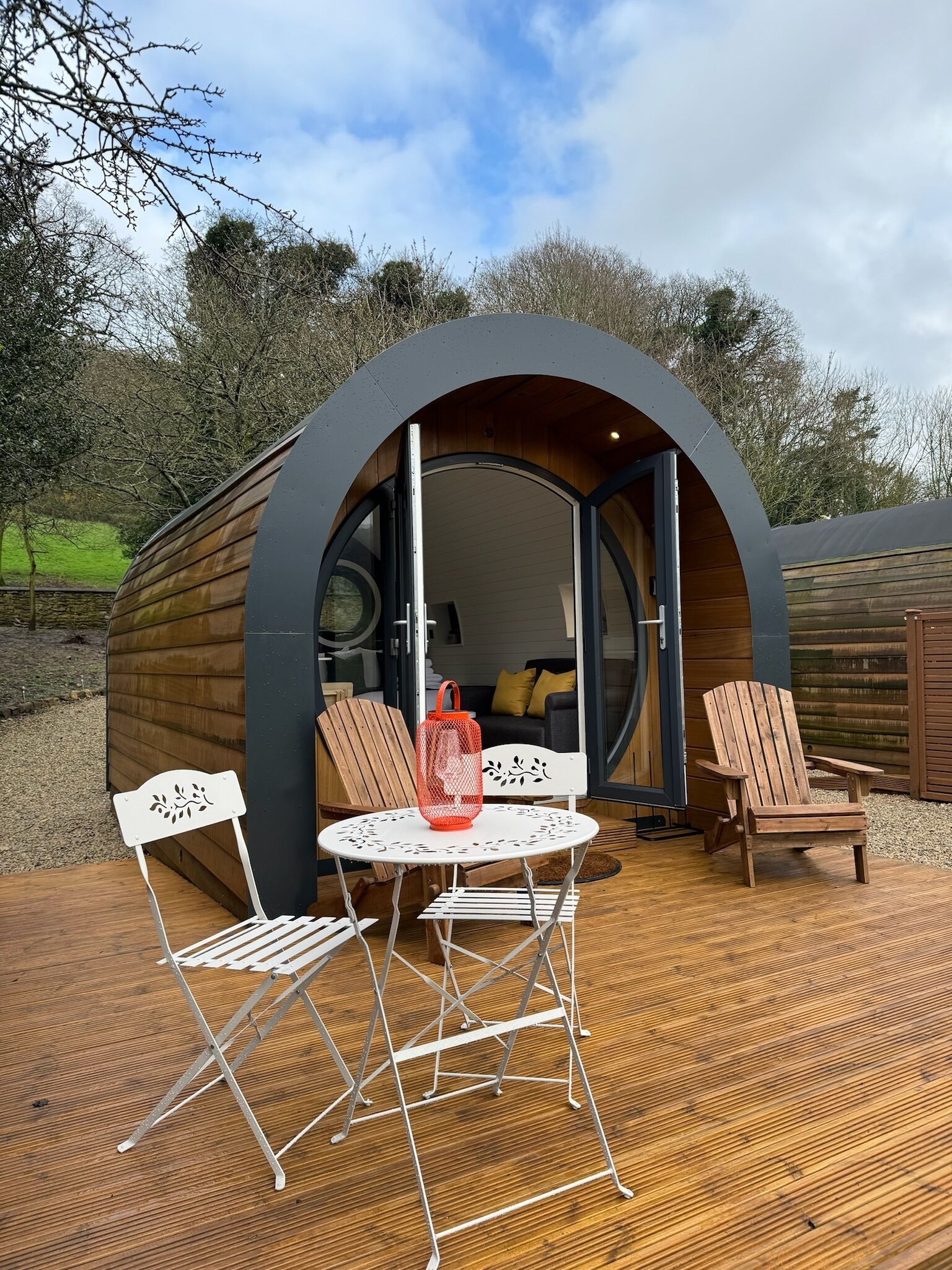 Un petit espace circulaire et chaleureux, fait de bois, doté d’une porte coulissante et aménagé avec une table blanche, deux chaises et une lanterne rouge.