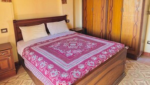 A bedroom with a wooden bed, a patterned bedspread, a wardrobe, and an arched doorway. - Ramses (Luxor)