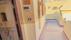 A narrow corridor with patterned floor tiles, a wooden door with a geometric design, and a small window with a lattice design. - Ramses (Luxor)