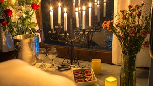Una mesa con velas, una copa de vino, un florero con flores y un plato de comida.
