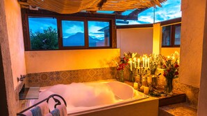 A bathroom with a large bathtub, a window with a view of mountains, and a decorative arrangement of candles and flowers.