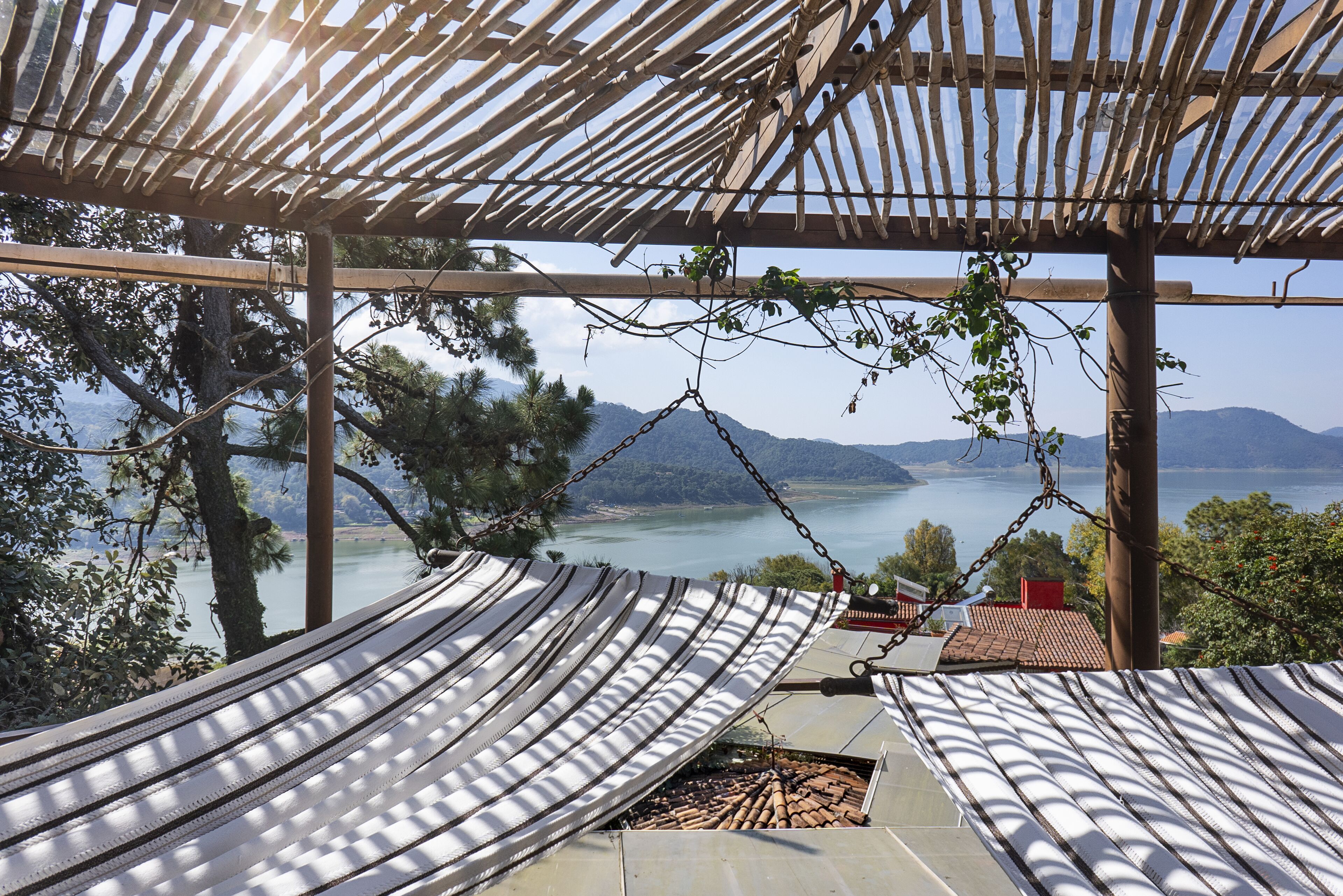 Un hamac suspendu sous une pergola en bambou, d’où l’on a vue sur un lac et, au loin, sur des montagnes.