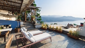 Una terraza con sillones, plantas en macetas y vistas al mar y a las montañas.