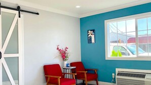 A room with two red chairs, a small table, a vase with flowers, a window with a view of cars, and a sliding door. - Motel6 Yuba City, CA (Yuba City)