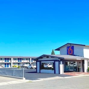 A motel with a prominent '6' sign, a covered parking area, and a row of motel units in the background. - Motel6 Yuba City, CA (Yuba City)
