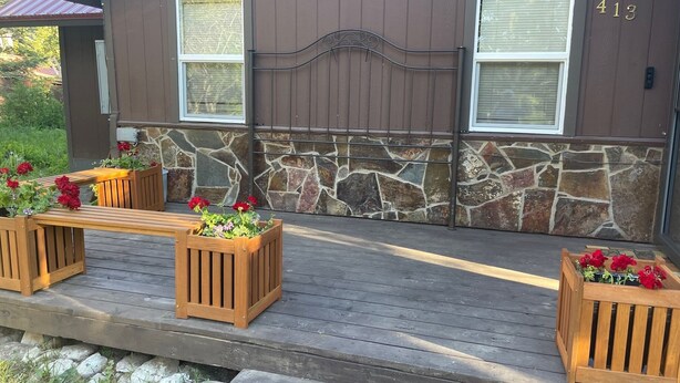 A wooden deck with built-in planters containing red flowers, a stone wall, and a house number 413.