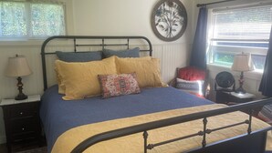 A bedroom with a bed, nightstands, a window with blinds, and a decorative wall piece.