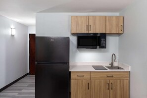 Eine kleine Küche mit einem schwarzen Kühlschrank, einer Mikrowelle und Holzschränken.