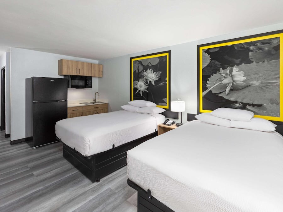 A hotel room with two beds, a refrigerator, a microwave, a wooden cabinet, a sink, and two large floral paintings.