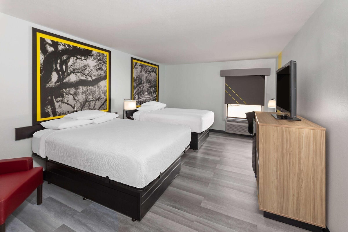 A hotel room with two beds, a TV, a desk, and artwork on the walls.