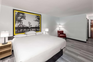 A hotel room with a large bed, a red chair, two bedside lamps, and a framed picture on the wall. - Super 8 by Wyndham Alexandria LA (Alexandria)