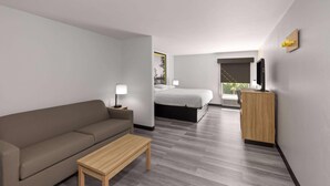 A modern hotel room with a sofa, a wooden table, a bed, a desk, and a TV. - Super 8 by Wyndham Alexandria LA (Alexandria)