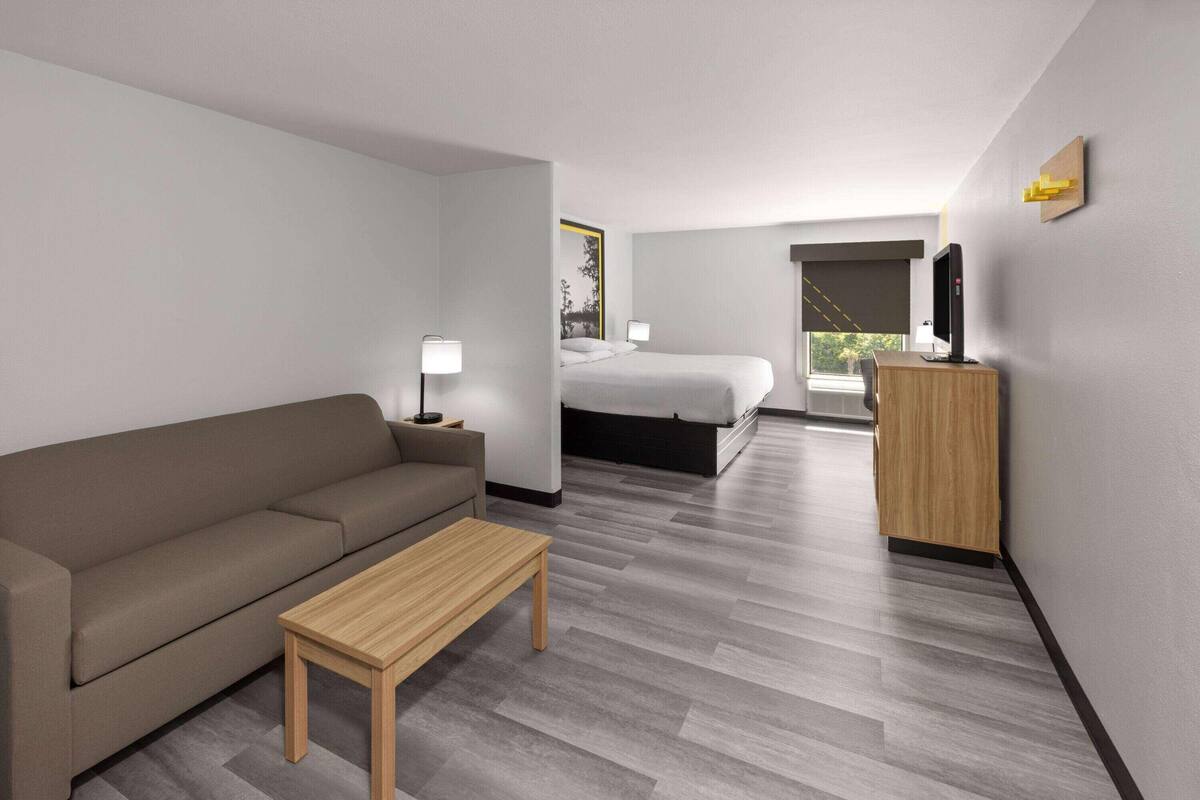 A modern hotel room with a sofa, a wooden table, a bed, a desk, and a TV.