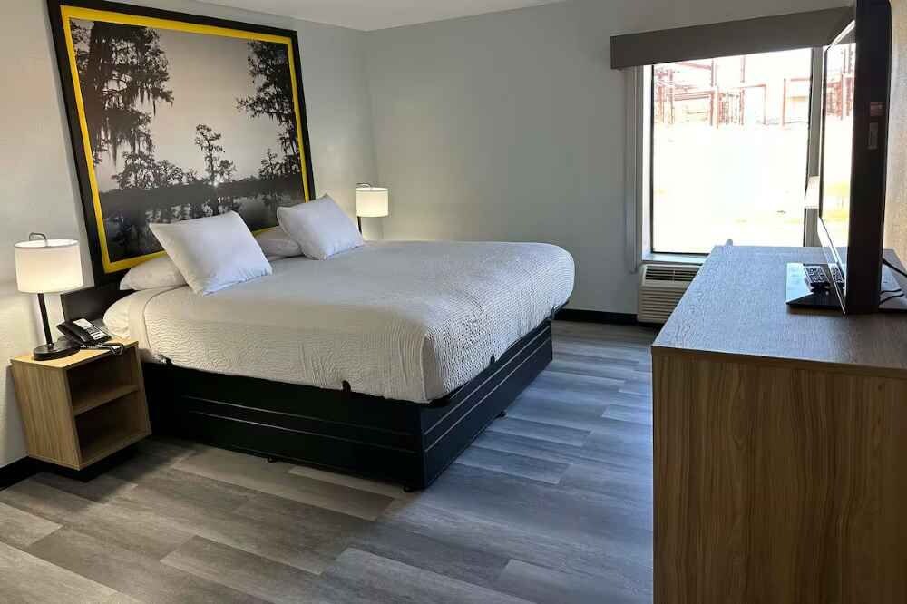 A hotel room with a bed, bedside lamps, a desk with a computer, and a large window.
