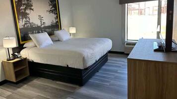A hotel room with a bed, bedside lamps, a desk with a computer, and a large window.