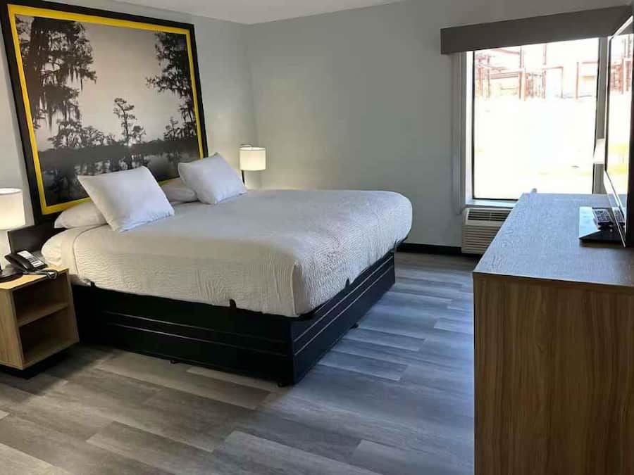 Habitación de hotel con cama, lámparas de noche, un escritorio con ordenador y un ventanal grande.