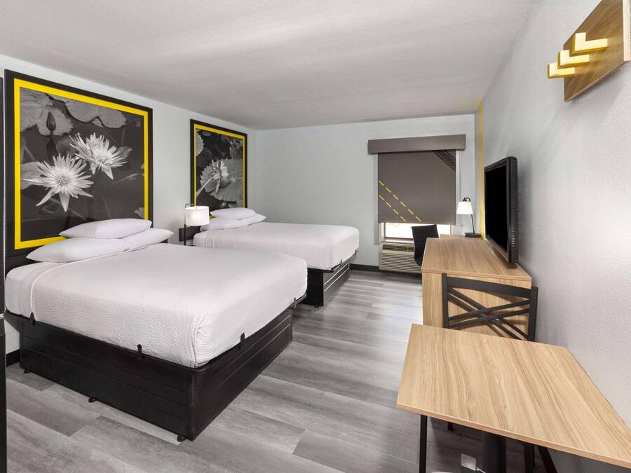 A hotel room with two beds, a desk, a TV, and artwork on the walls.