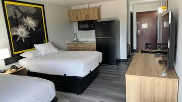 A hotel room with a bed, a desk, a microwave, a refrigerator, and a bathroom.