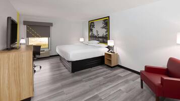 A hotel room with a bed, a desk with a flat-screen TV, a red chair, and a painting on the wall.