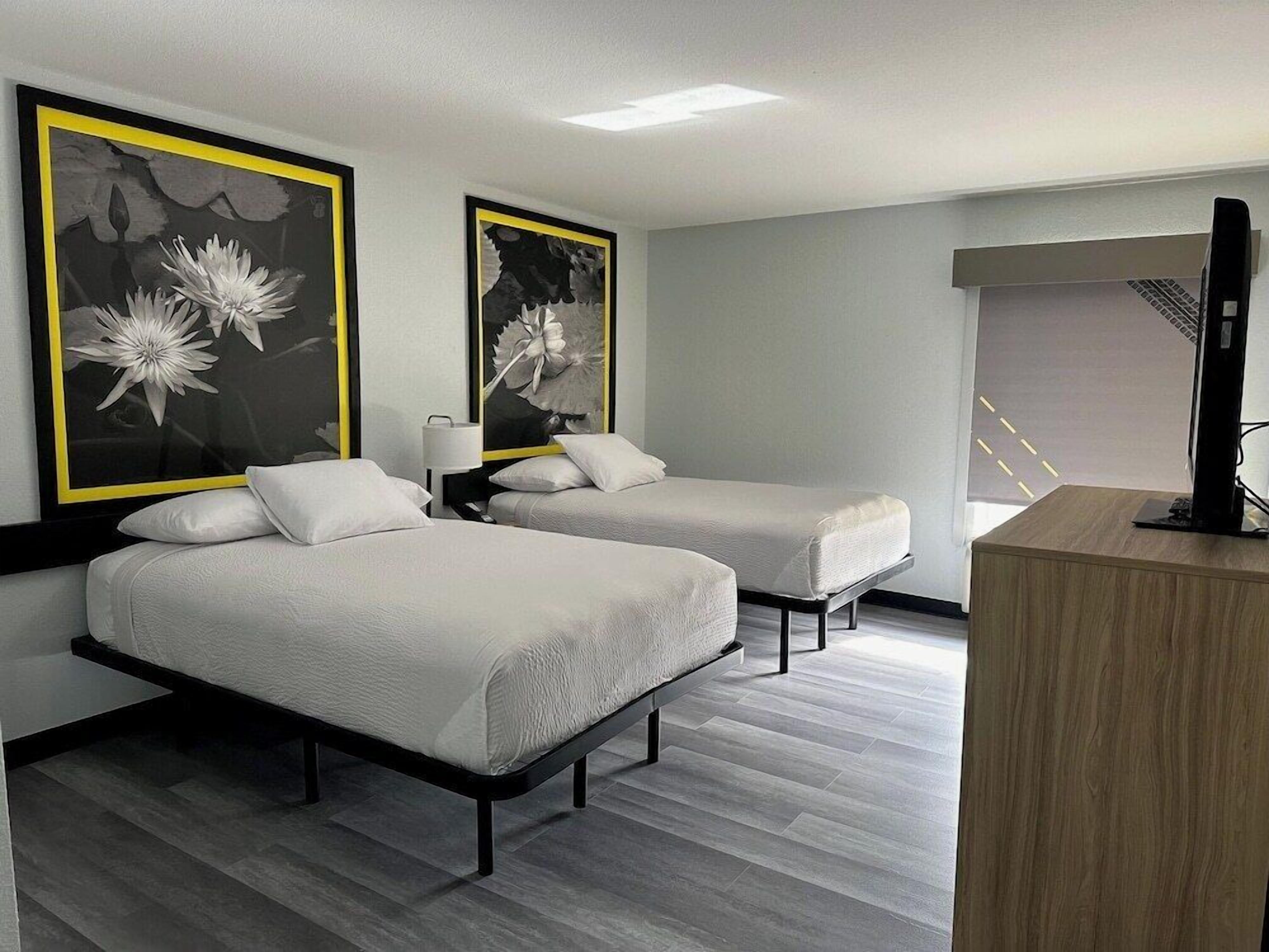 A hotel room with two beds, a desk, and artwork on the walls.