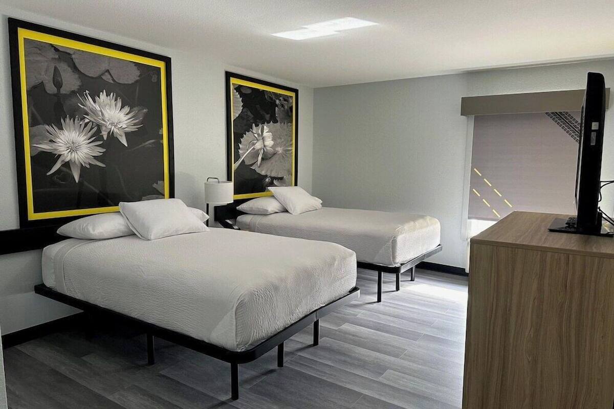 A hotel room with two beds, a desk, and artwork on the walls.