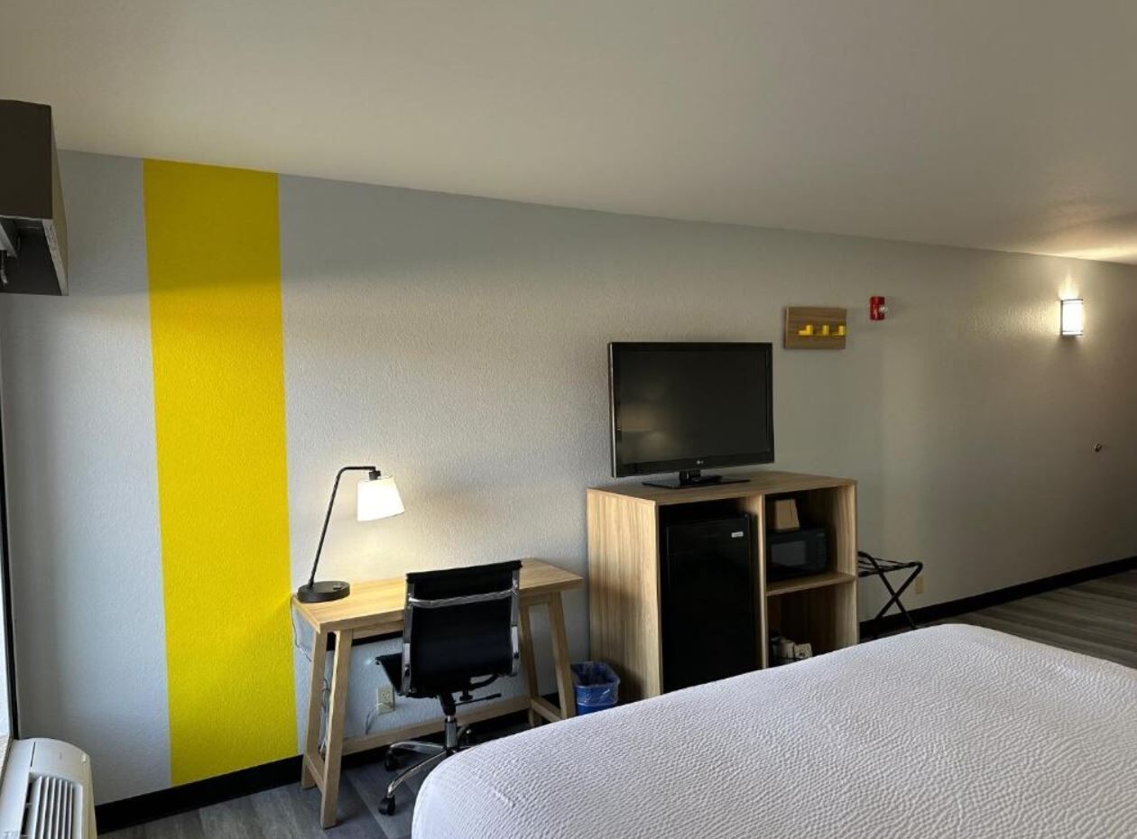 A hotel room with a bed, a desk with a chair, a television, and a small cabinet.