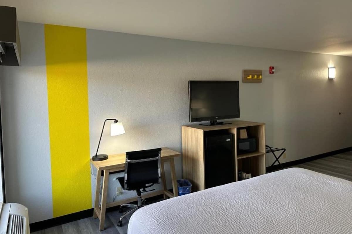 A hotel room with a bed, a desk with a chair, a television, and a small cabinet.