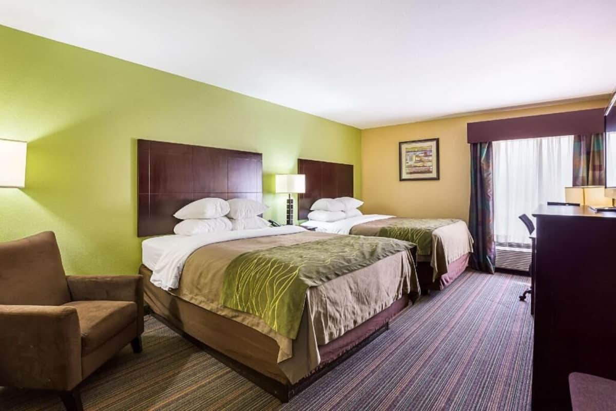 A hotel room with two beds, a desk, a chair, and a window with curtains.