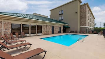 A poolside area with lounge chairs, a swimming pool, and a building with a brick facade and large windows.