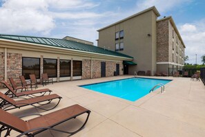A poolside area with lounge chairs, a swimming pool, and a building with a brick facade and large windows. - Super 8 by Wyndham Alexandria LA (Alexandria)