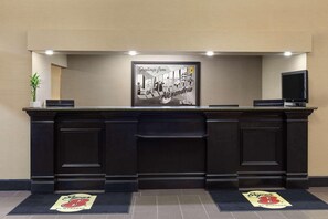 A reception desk with a framed welcome sign, a potted plant, and a flat-screen TV. - Super 8 by Wyndham Alexandria LA (Alexandria)