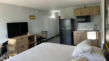 A hotel room with a bed, a TV, a desk, a chair, a refrigerator, a microwave, and a sink.