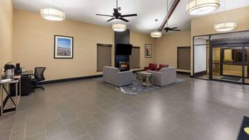 A lobby with a fireplace, ceiling fans, and a seating area with chairs and a table.