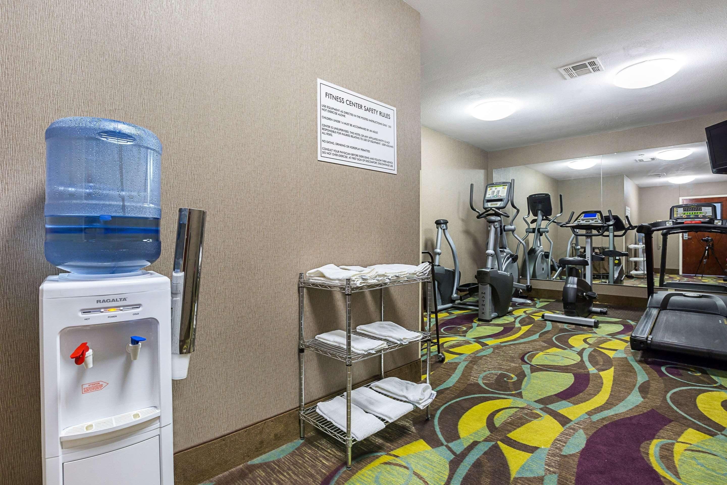 A fitness center with exercise equipment, a water dispenser, and a sign detailing safety rules.