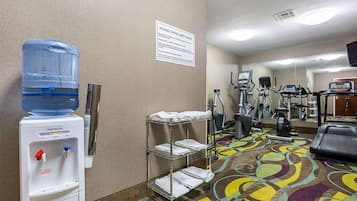 A fitness center with exercise equipment, a water dispenser, and a sign detailing safety rules.