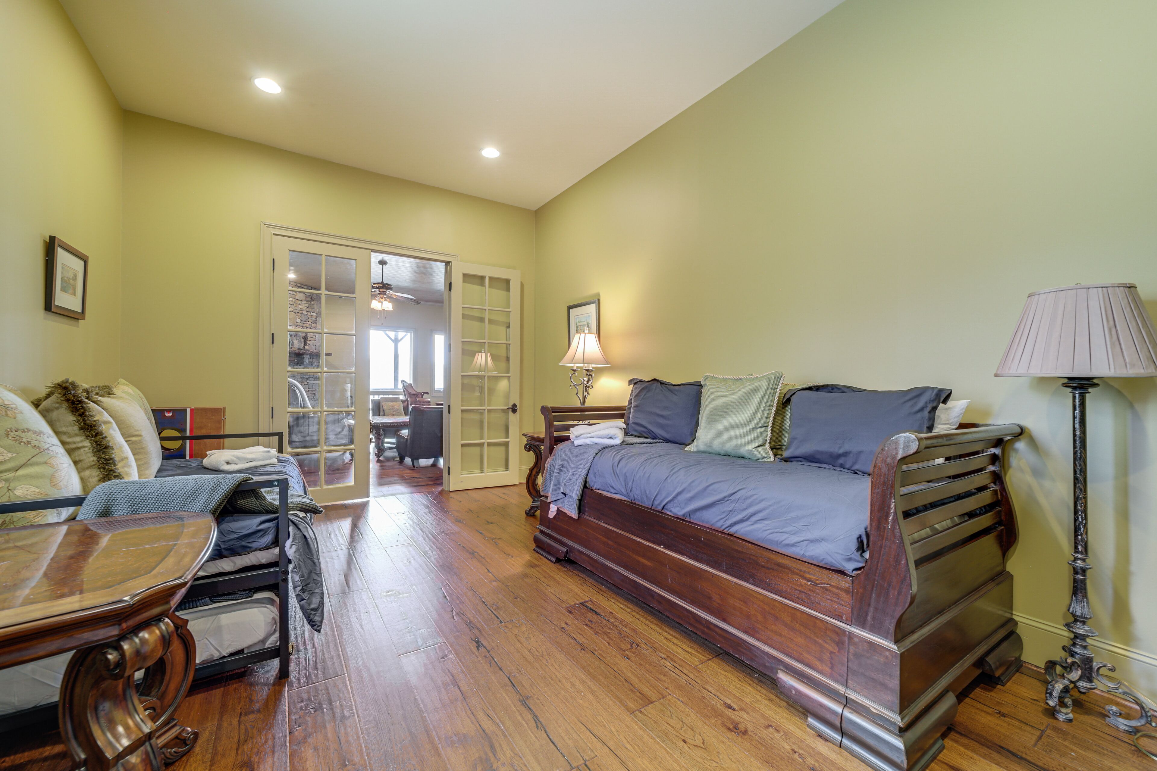 A bedroom with a wooden bed, a desk, and a chair. There is a door leading to another room.