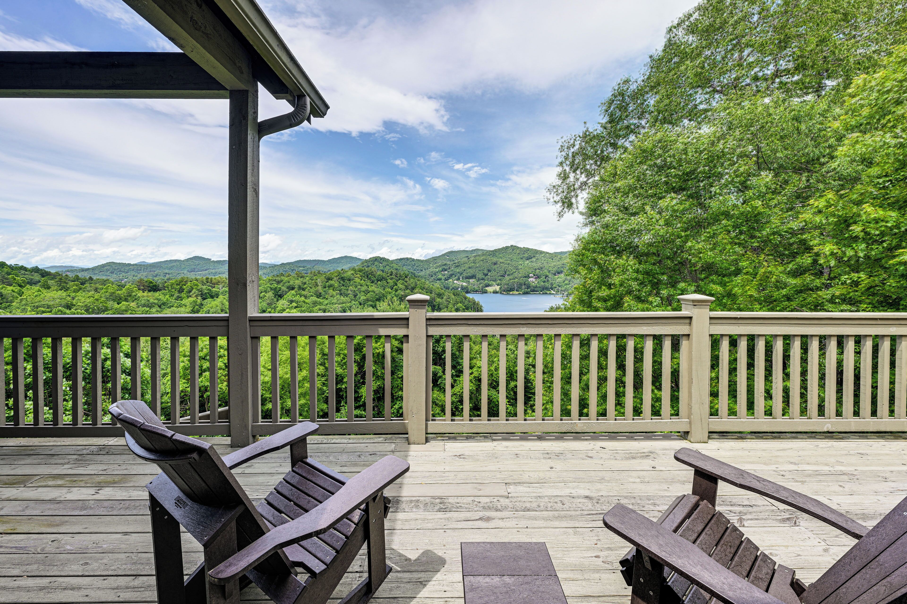 Una terraza de madera con sillas Adirondack con vistas a un lago y colinas boscosas.
