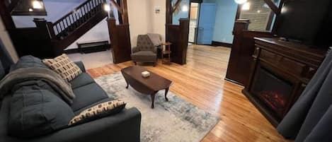 A living room with a dark-colored sofa, a coffee table, and a fireplace. There is a staircase leading to another room.