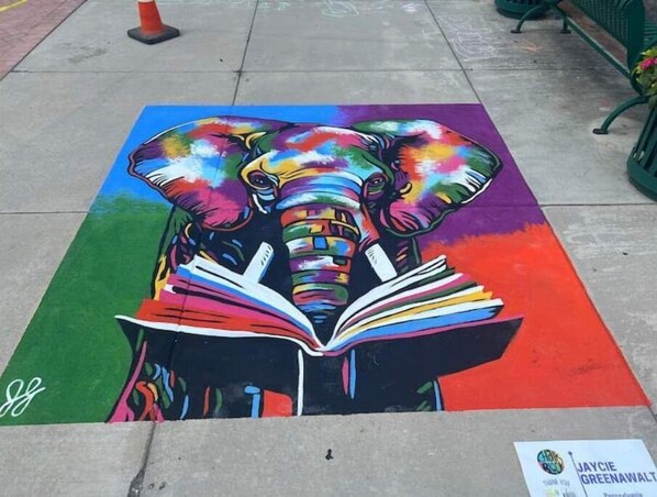 A colorful street art of an elephant reading a book.