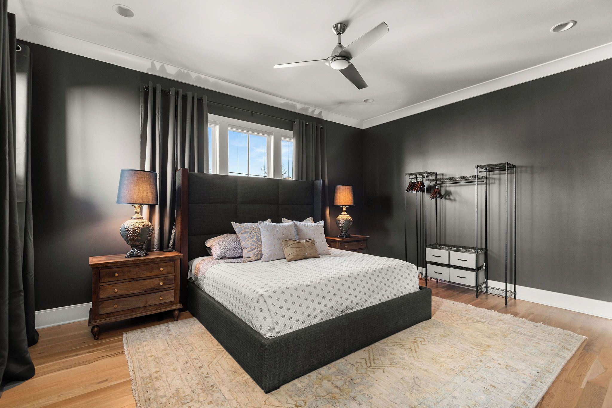 A bedroom with a bed, two nightstands, a ceiling fan, a window with curtains, and a storage unit.