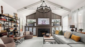 A spacious living room with a fireplace, a large television, and a high ceiling with a chandelier. - The Blue Note - Luxe Outdoor Retreat & Pool - Close to Downtown (Nashville)