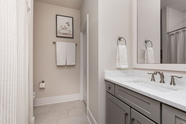 Un bagno con un lavandino bianco, due portasciugamani, un quadro appeso al muro e un water con un rotolo di carta igienica.