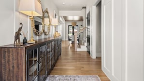 A hallway with a wooden floor, a dark wooden console with glass doors, and a large mirror with a gold frame. - The Blue Note - Luxe Outdoor Retreat & Pool - Close to Downtown (Nashville)
