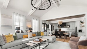 A modern living room with a grey sectional sofa, a coffee table, and a dining area with a kitchen in the background. - The Blue Note - Luxe Outdoor Retreat & Pool - Close to Downtown (Nashville)
