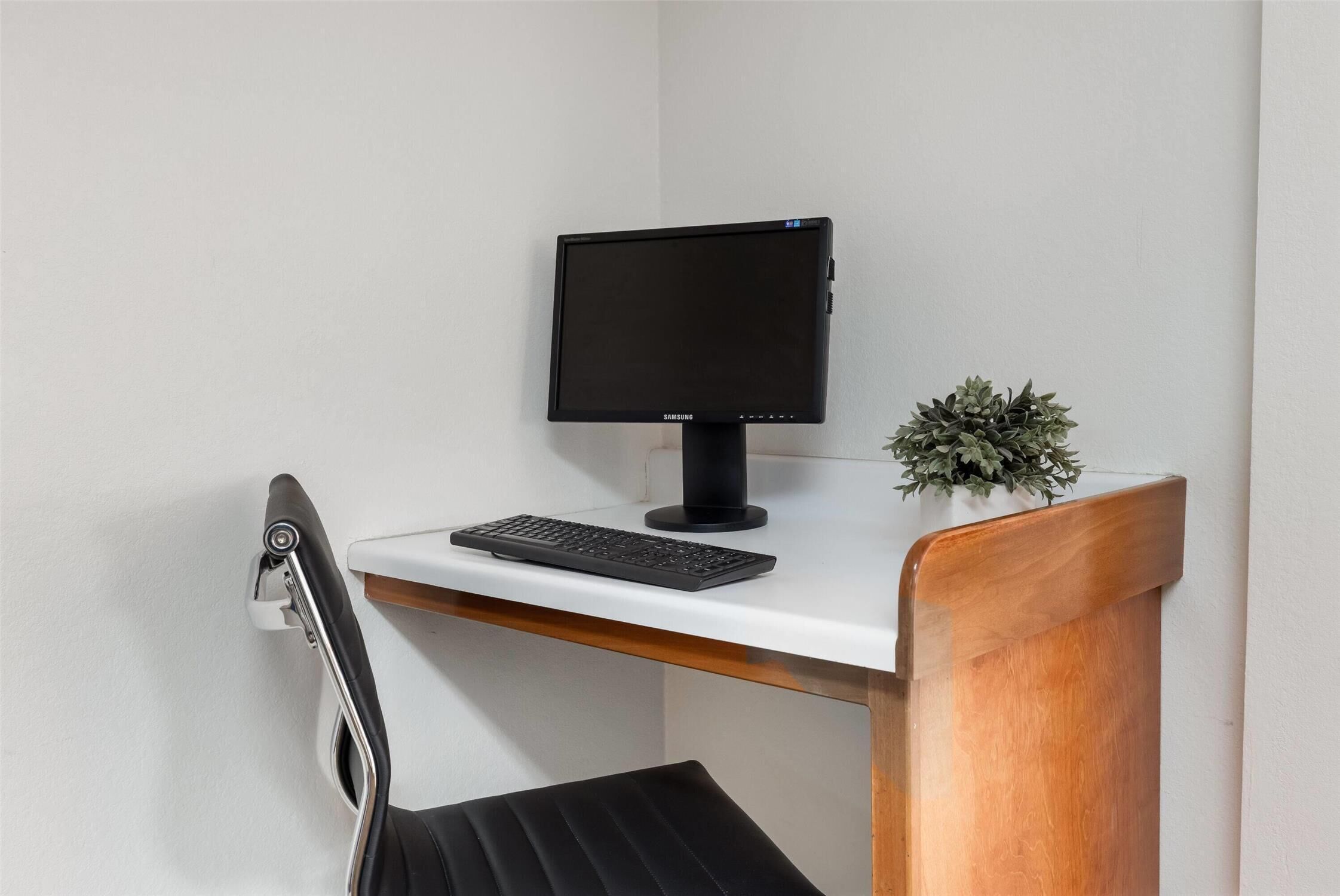 A modern desk with a computer monitor, keyboard, and a small potted plant.